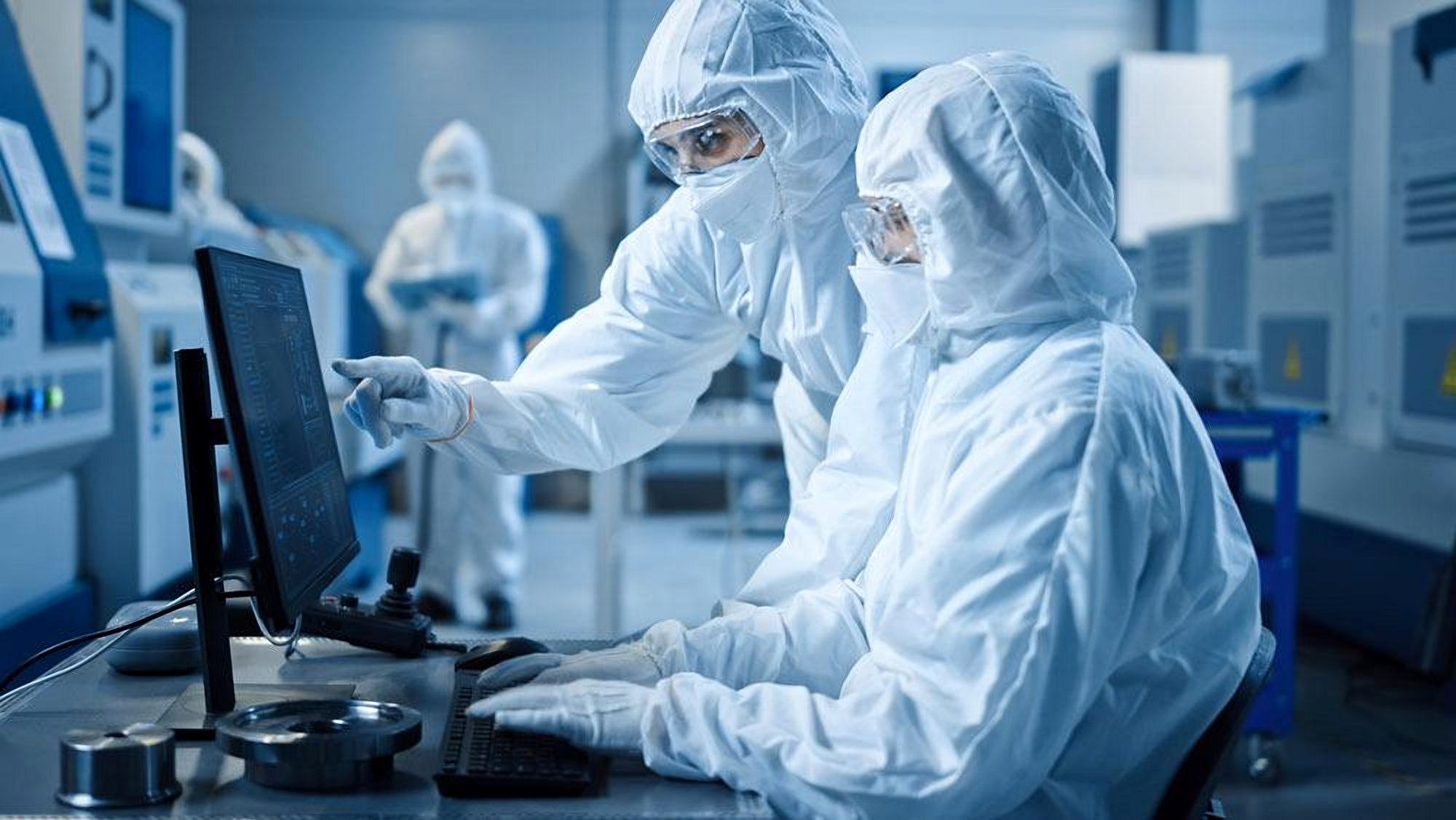 Two technicians in cleanroom suits reviewing data at a workstation